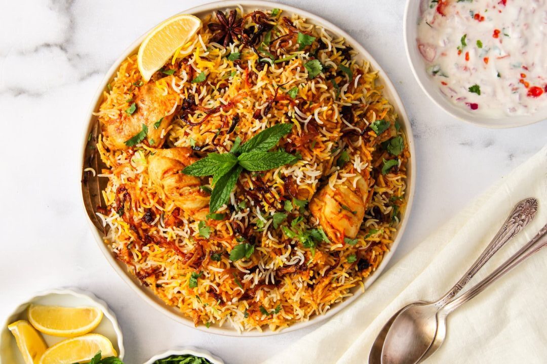 A plate of chicken biryani garnished with cilantro and lemon.