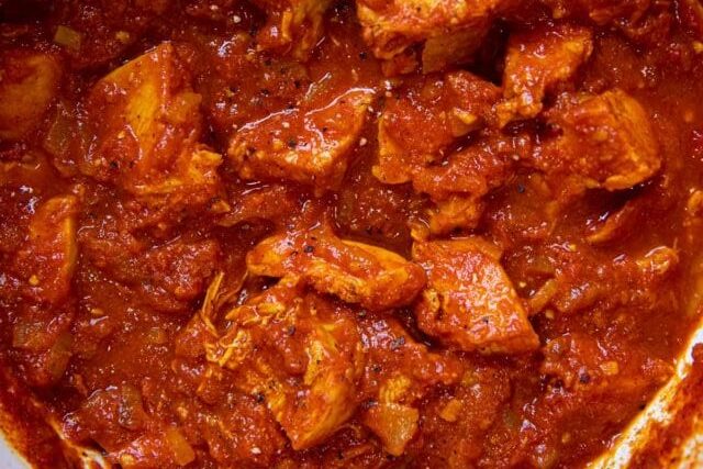 Close-up of marinated chicken in red spices and sauce.