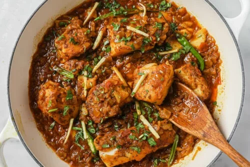 Spicy chicken curry garnished with fresh herbs served in a wooden bowl.
