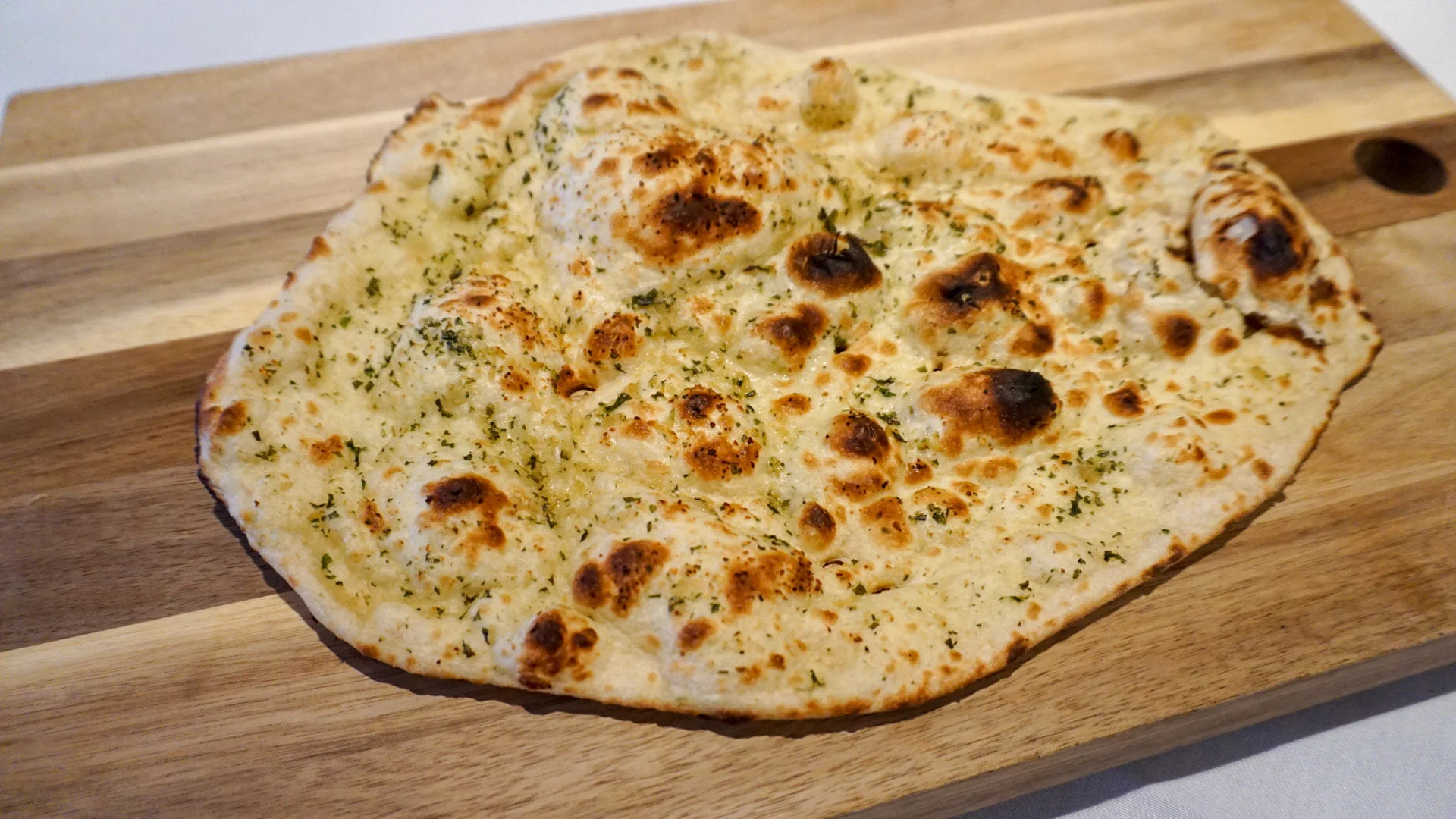 Freshly baked garlic naan bread with herbs on a wooden board.