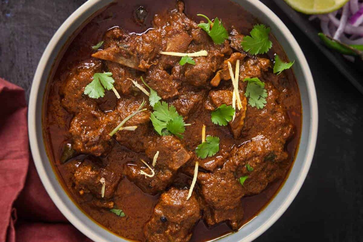 A bowl of rich, spiced meat curry garnished with cilantro and ginger.