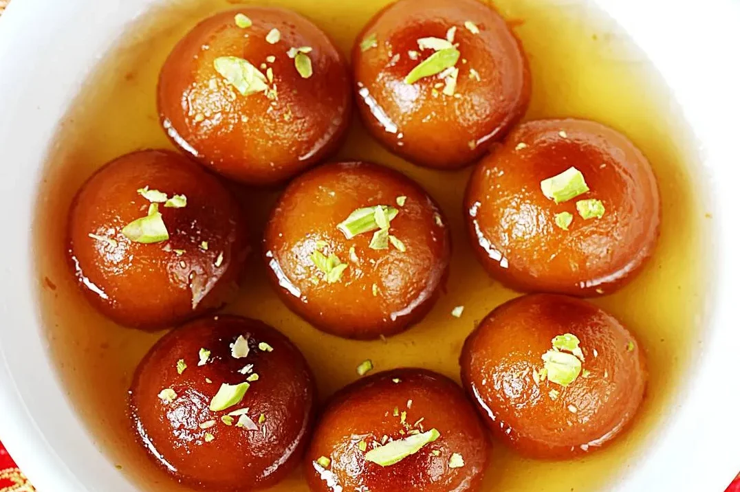 Delicious gulab jamuns garnished with pistachios in syrup.