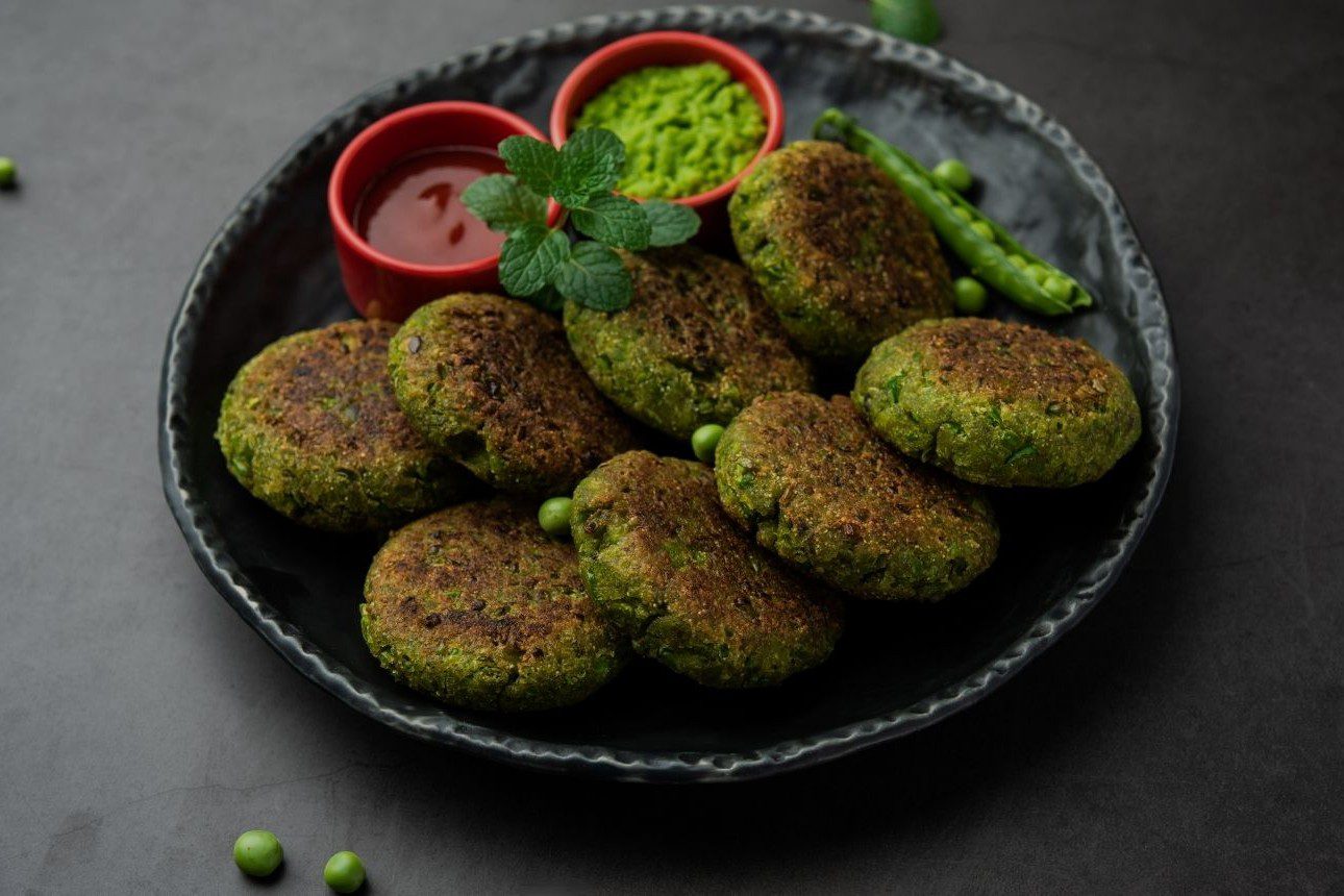 Plate of green vegetable cutlets garnished with ketchup and green chili.