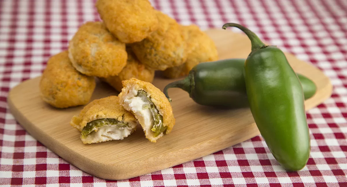 Breaded jalapeño poppers on a wooden board with fresh jalapeños.
