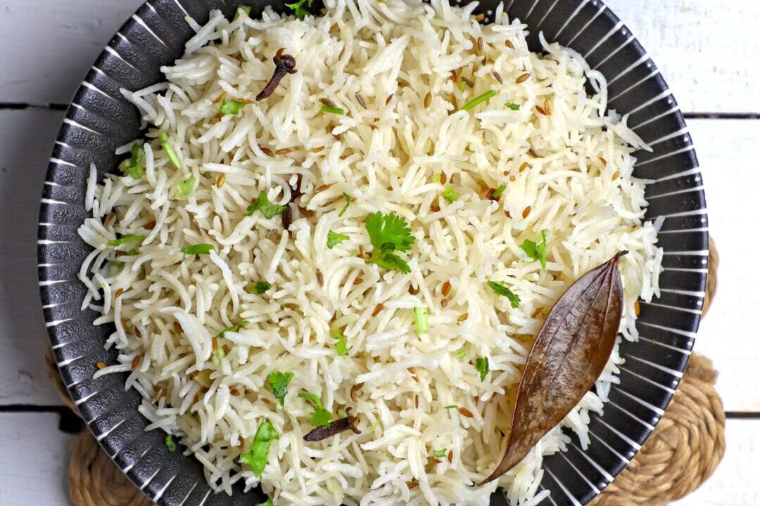 A bowl of cooked basmati rice garnished with bay leaf and peas.