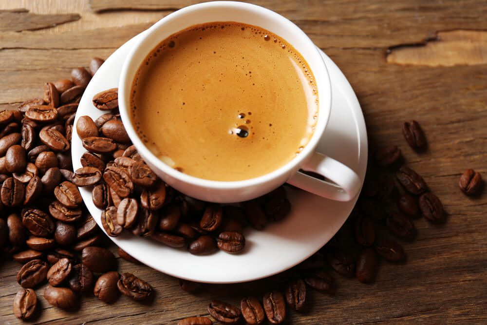 A cup of espresso with coffee beans on a wooden table.