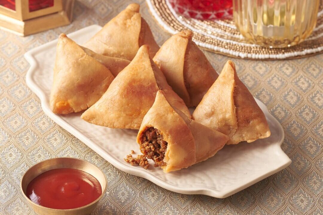 Plate of crispy samosas with chutney on the side.