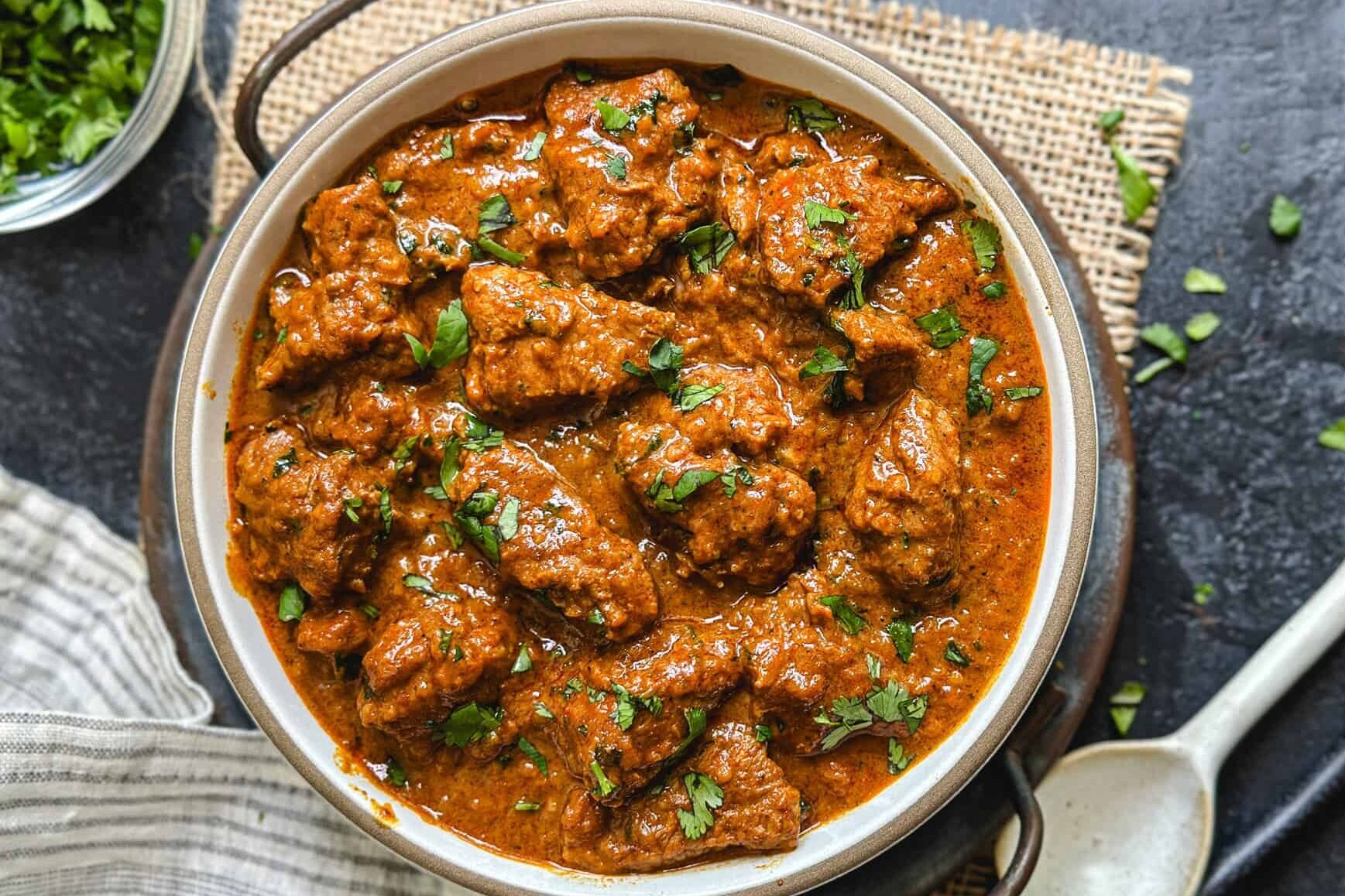 A bowl of rich, spicy chicken curry garnished with fresh herbs.