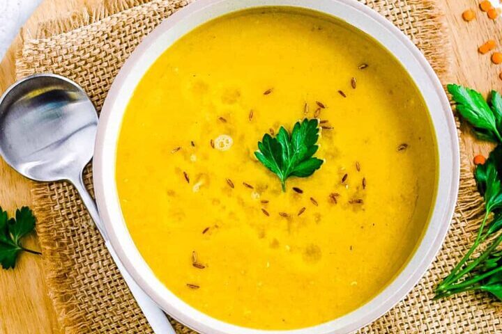 Creamy pumpkin soup garnished with parsley and seeds in a white bowl.