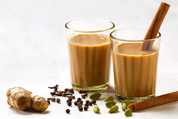 Two glasses of chai tea with spices on a white surface.