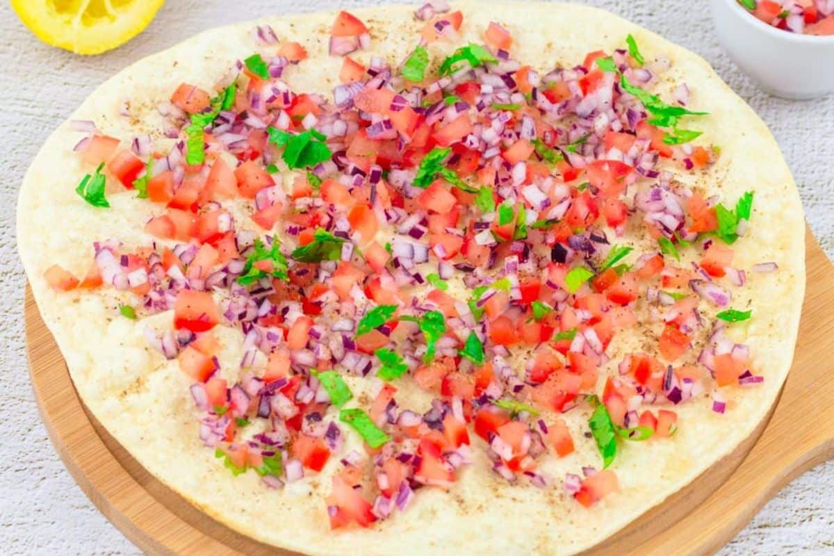 A colorful bruschetta topped with diced tomatoes, onions, and herbs.