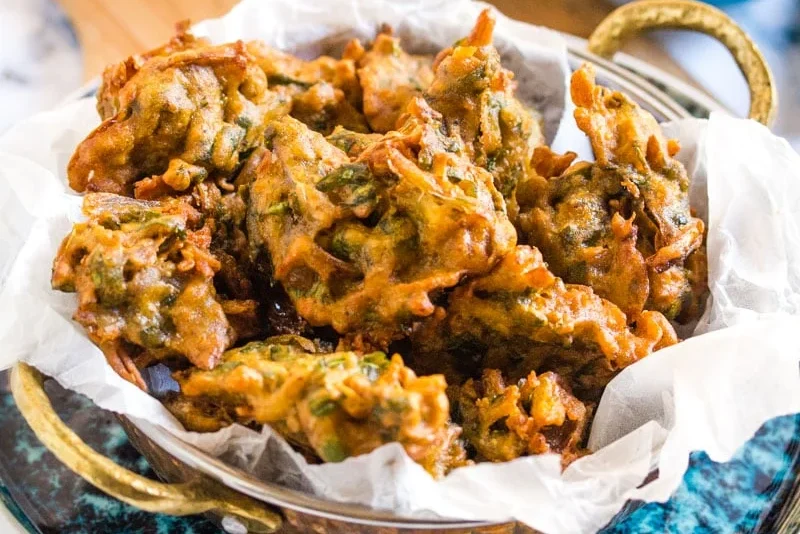 A plate of crispy vegetable pakoras with green herbs.