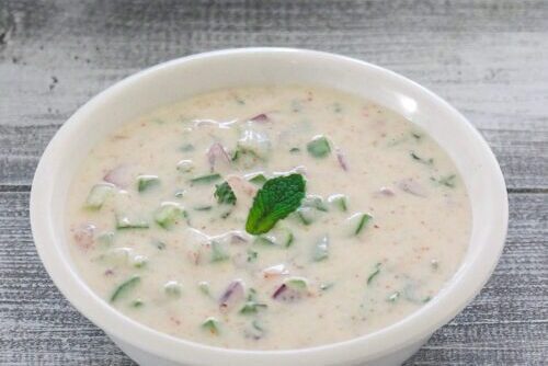 A bowl of creamy raita garnished with a mint leaf.