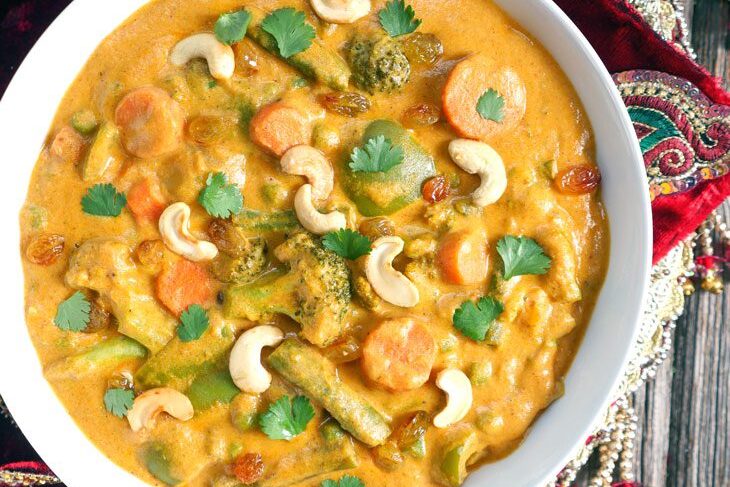 A bowl of creamy vegetable curry garnished with cashews and cilantro.