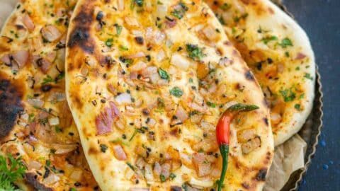Close-up of a cheesy pizza with chicken, herbs, and a chili pepper.