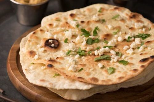 Freshly baked naan bread garnished with herbs on a wooden board.