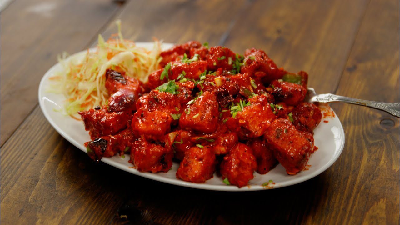 Plate of spicy, saucy chicken tikka garnished with herbs.