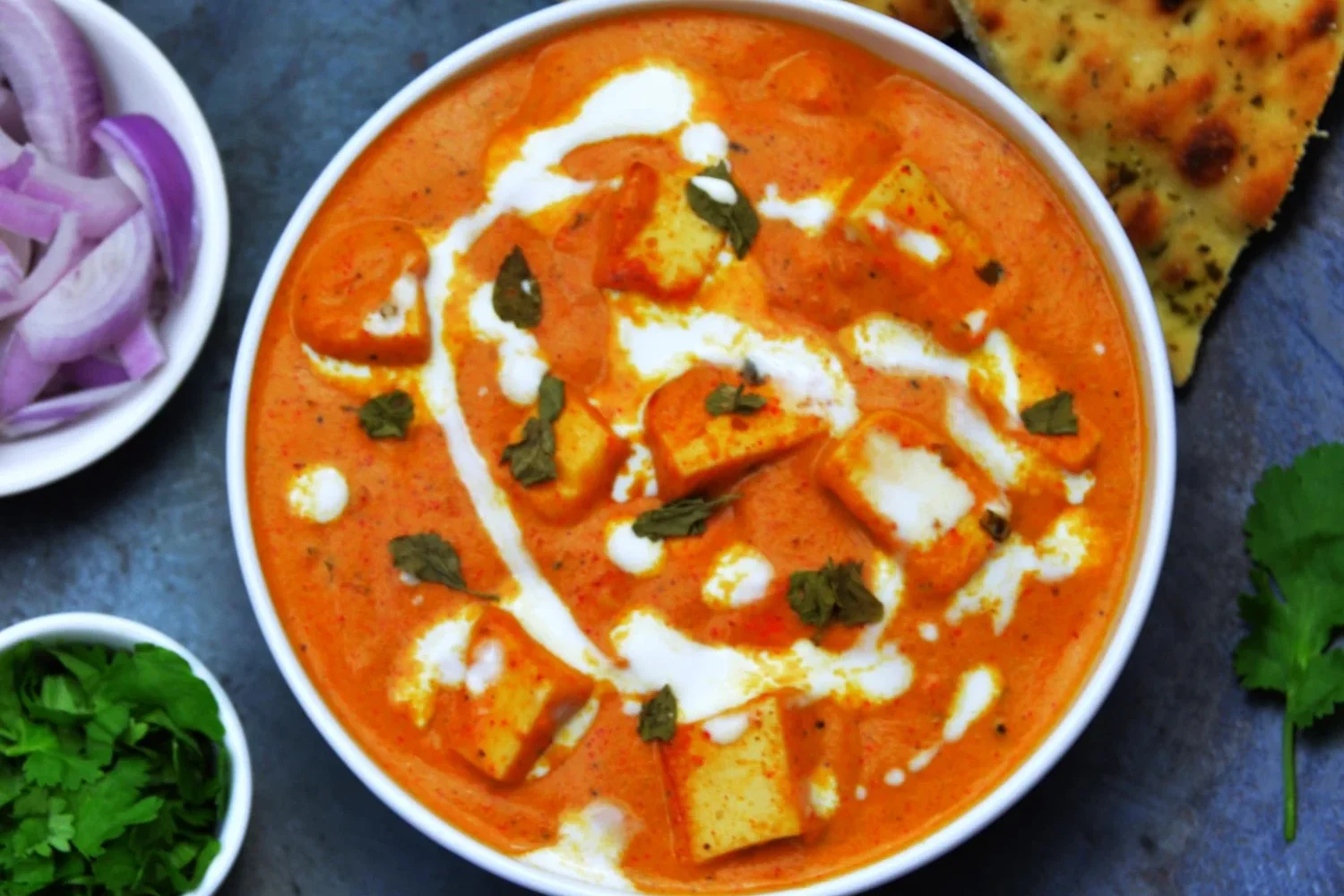 A bowl of creamy paneer butter masala garnished with cream and herbs.