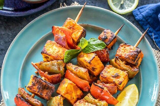 Grilled chicken and vegetable skewers with fresh basil on a blue plate.