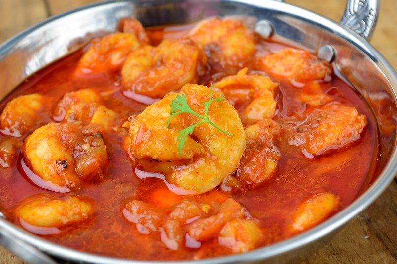 A bowl of spicy shrimp curry garnished with herbs.