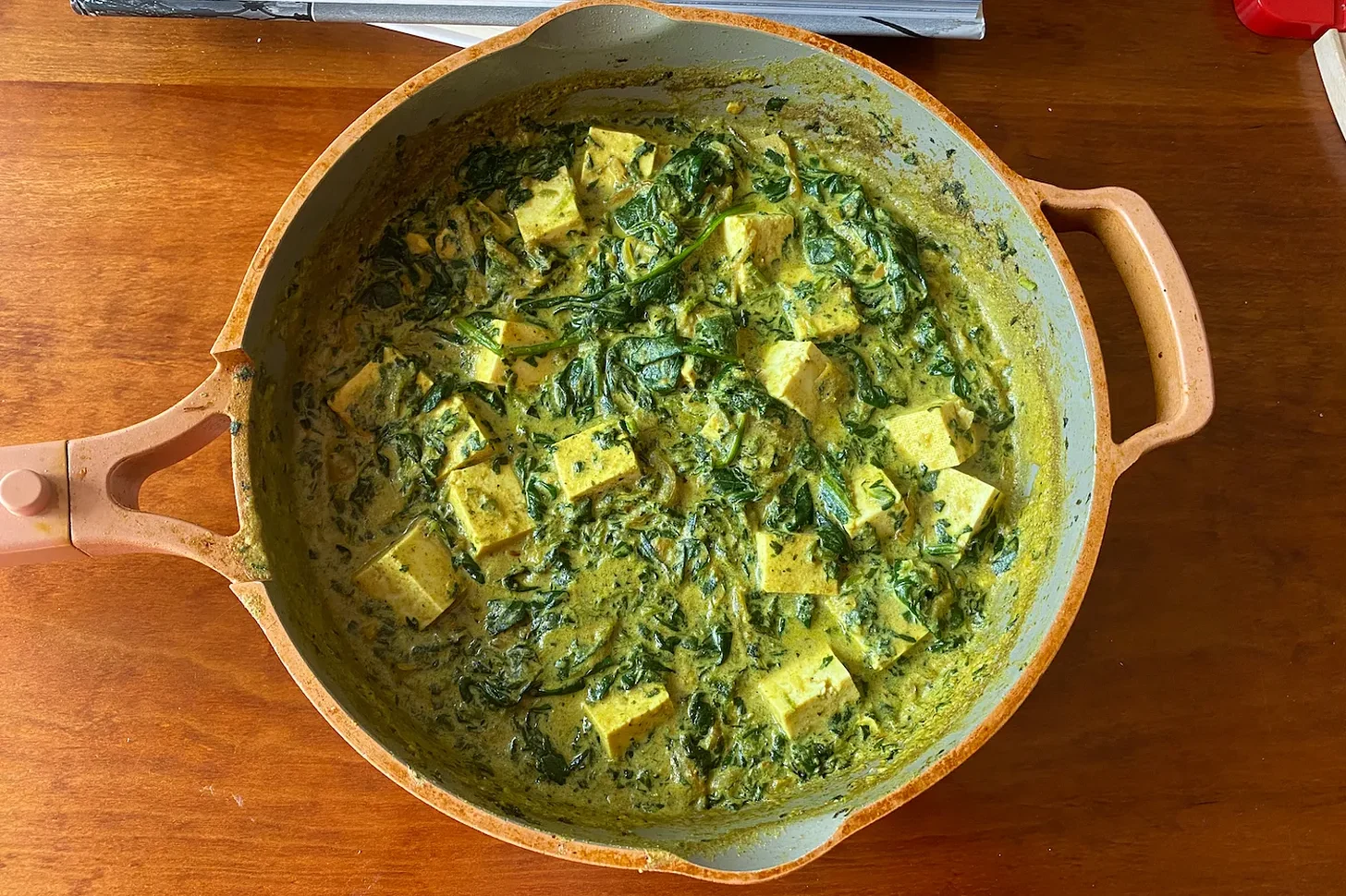 Bowl of green curry with paneer cubes.