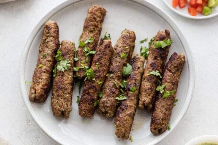 Grilled kofta kebabs garnished with fresh herbs on a white plate.