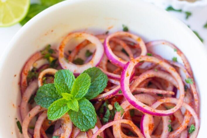 A bowl of sliced red onions garnished with fresh mint leaves.