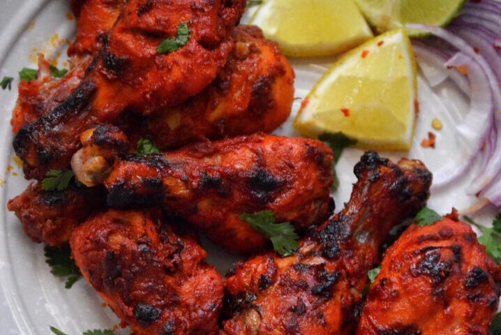 Close-up of grilled tandoori chicken with lemon wedges.