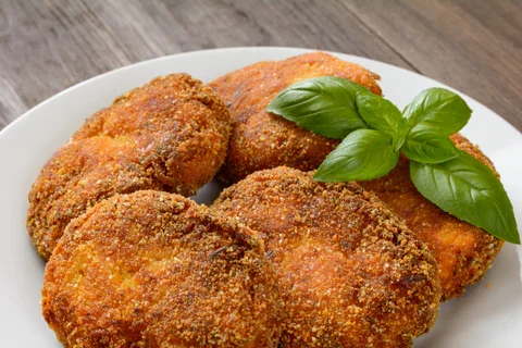 Golden-brown breaded patties with a tomato garnish and basil leaves.