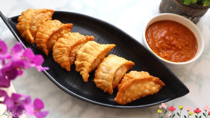 Golden fried dumplings arranged on a black plate with dipping sauce.