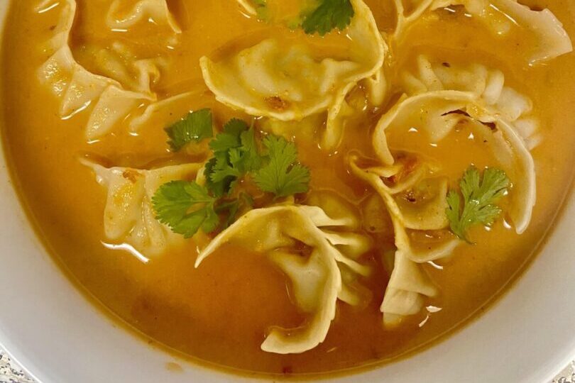 Close-up of tortellini pasta in broth with herbs.