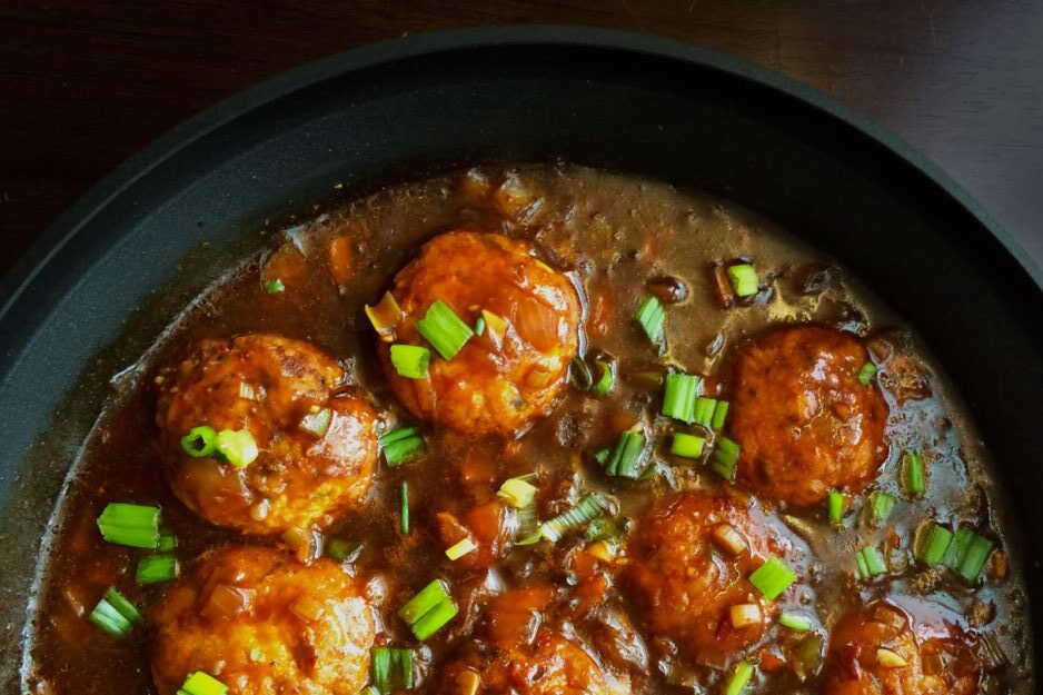 Spicy meatballs cooked in a rich sauce garnished with chopped green onions.