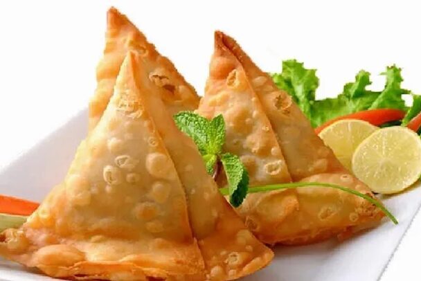 Golden fried samosas garnished with mint and lemon.