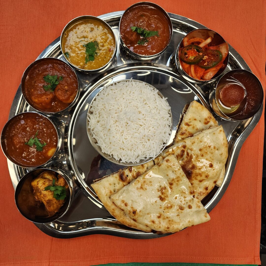 Traditional Indian thali with rice, naan, various curries, and sides.